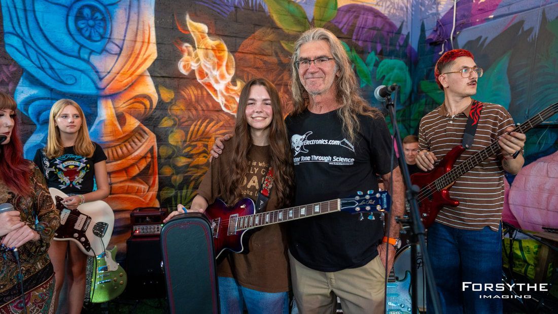 A group of people standing next to each other holding guitars in front of a mural.