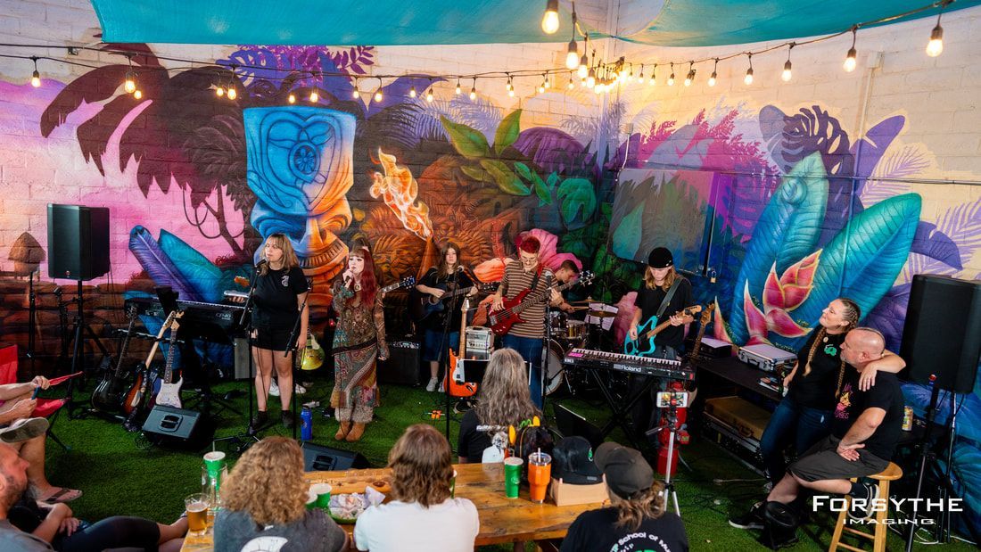 A group of people are sitting at tables watching a band perform on stage.