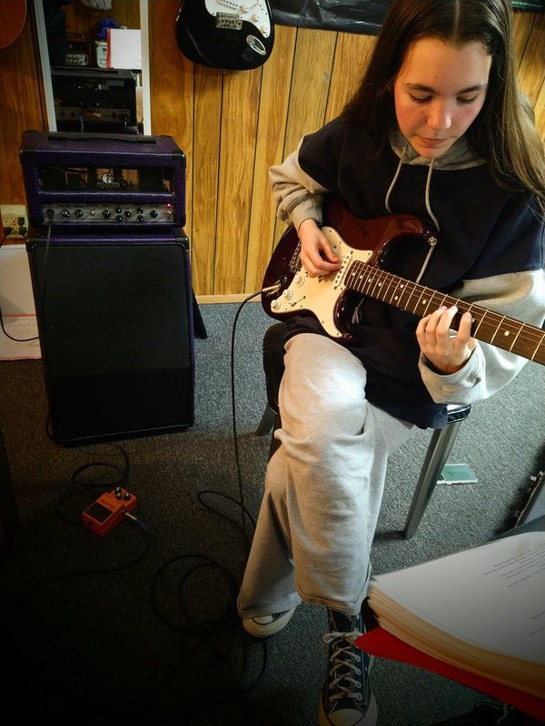 A girl is playing a guitar in front of a purple amplifier