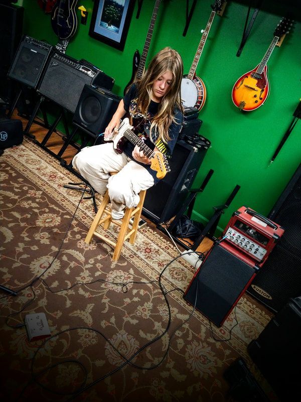 A woman is sitting on a stool playing a guitar