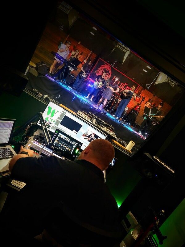 A man is sitting in front of a large screen watching a band on stage.