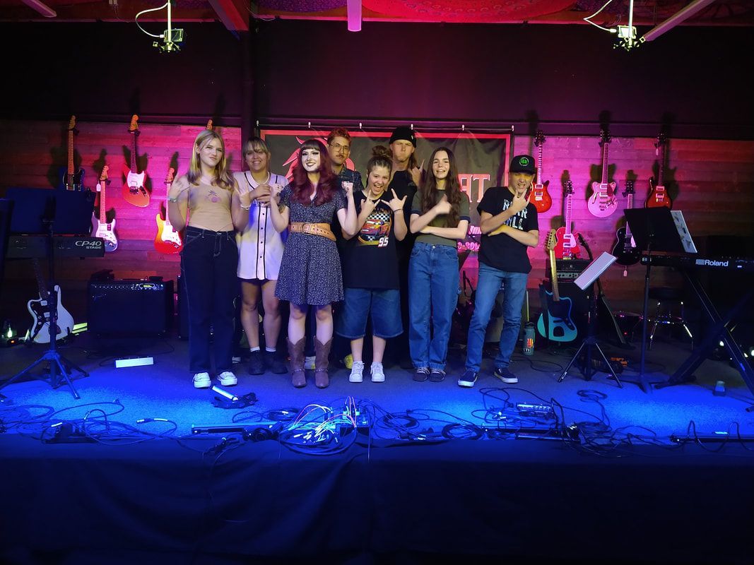 A group of people are standing on a stage in front of a wall of guitars.