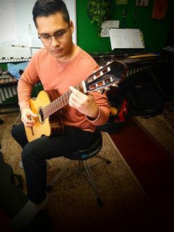 A man is sitting on a stool playing a guitar.