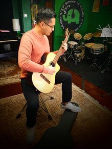A man is kneeling down playing a guitar in a room.