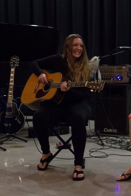 A woman is sitting on a chair playing an acoustic guitar