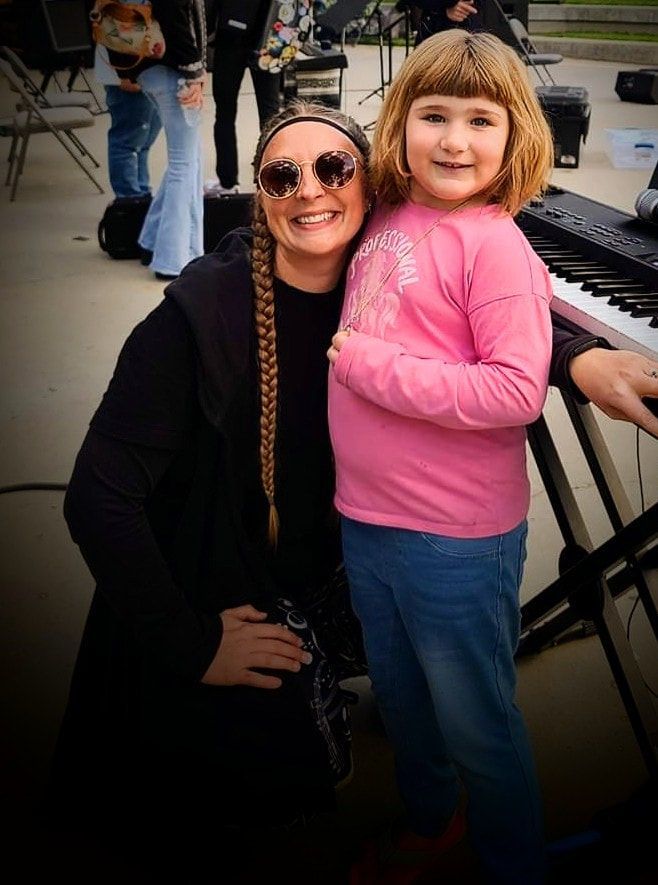 A woman and a little girl are posing for a picture in front of a piano.