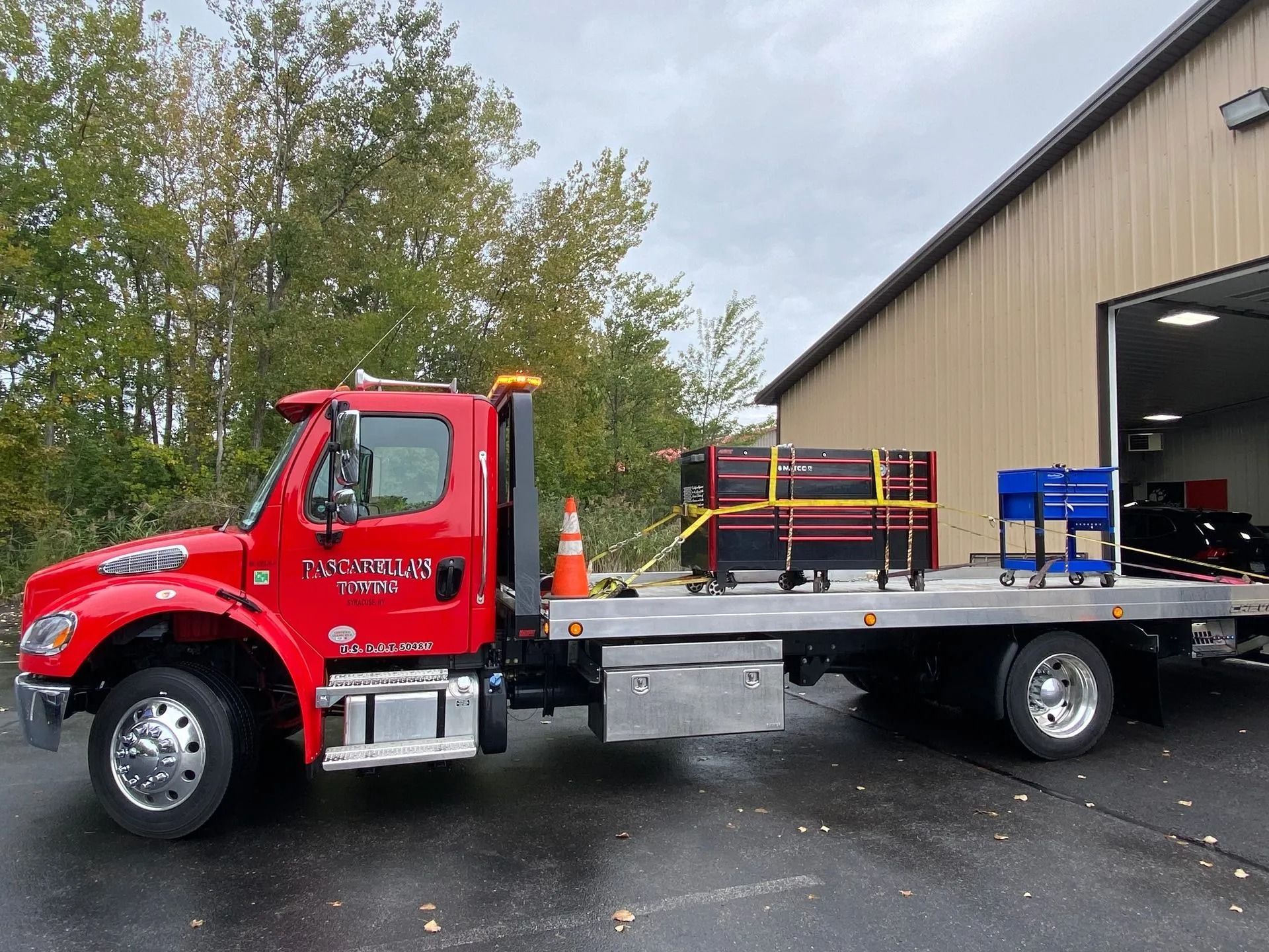 Red tow truck parked on a wet surface with tools on its flatbed near a building.