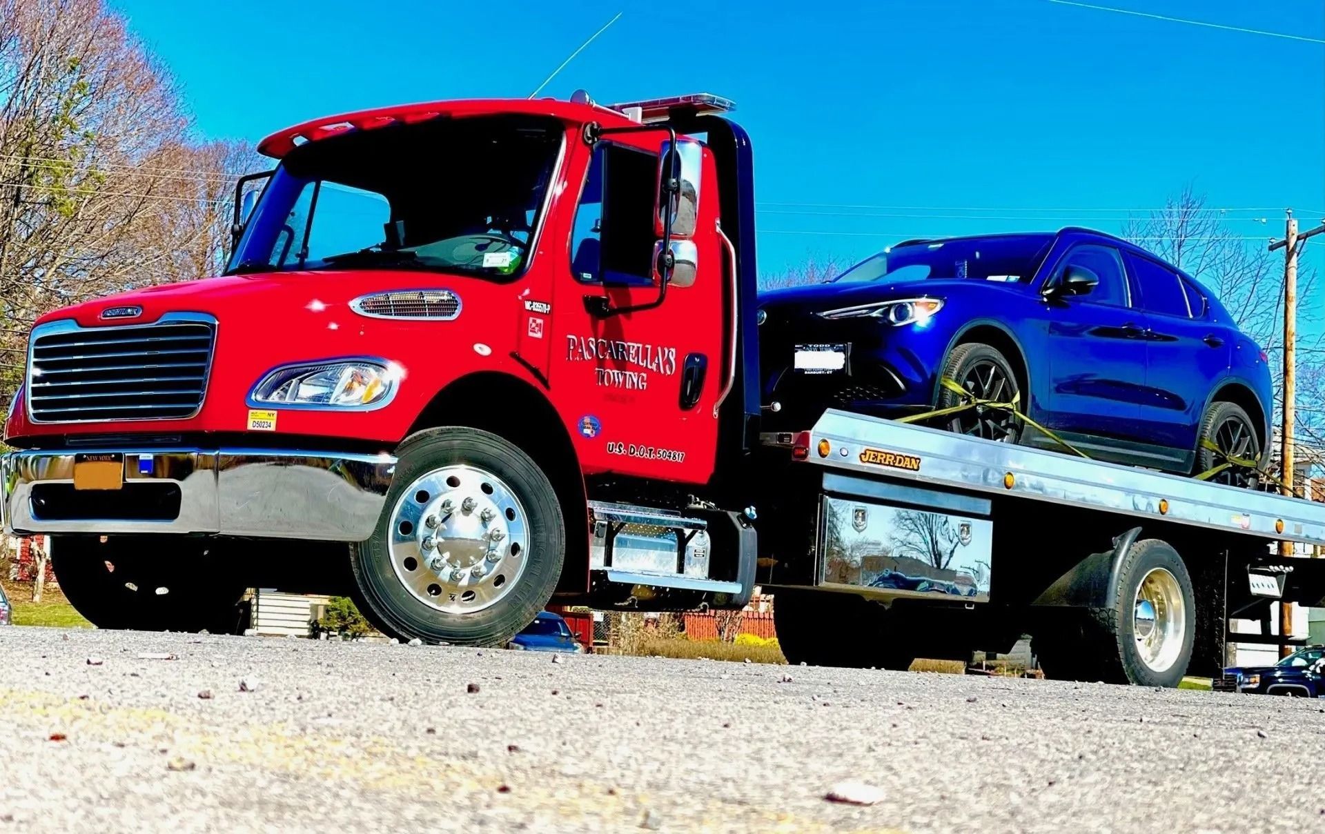 Red tow truck with a blue SUV on its flatbed, under a blue sky.