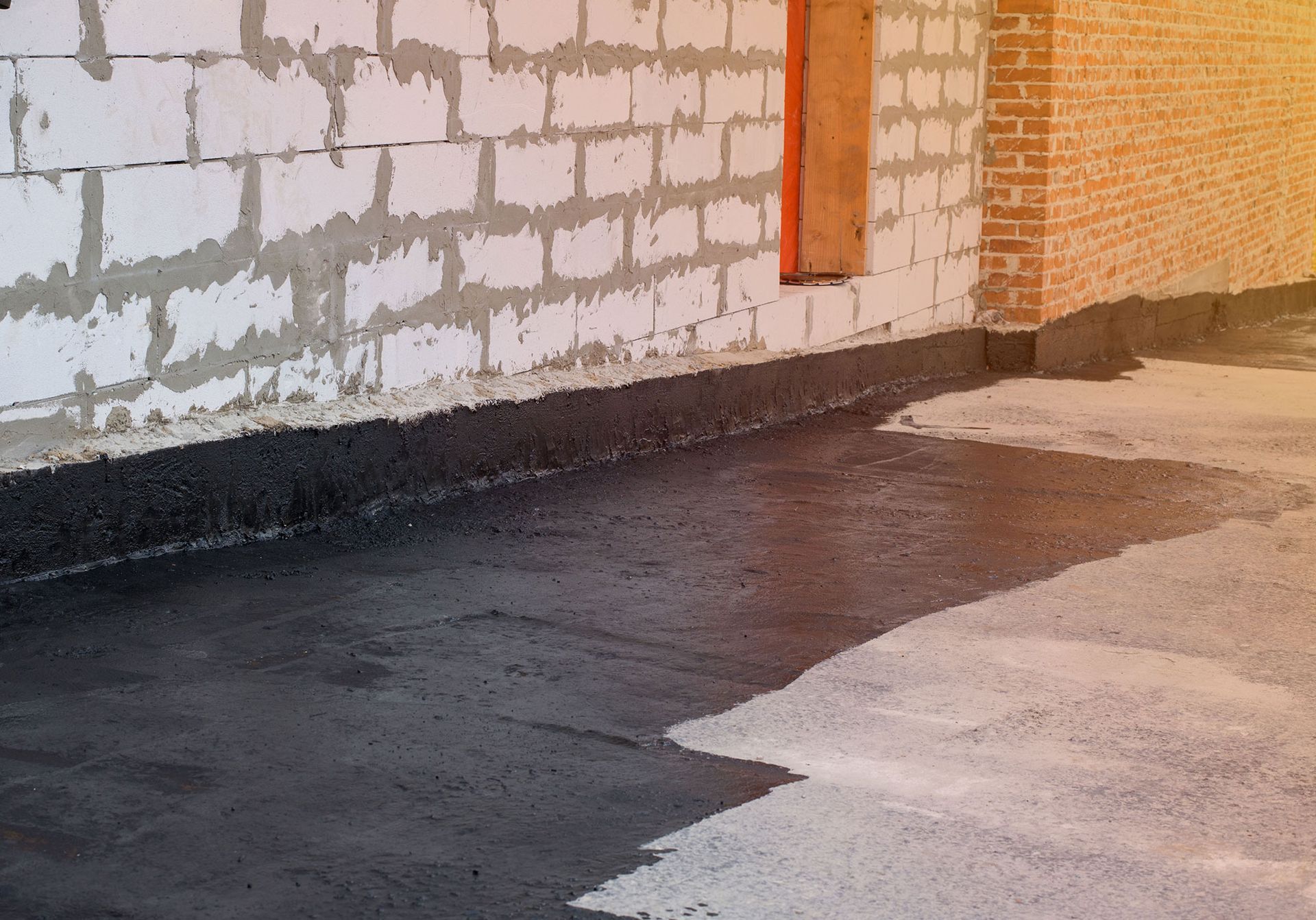 Black sealant applied on floor, against cinder block and brick walls during construction.