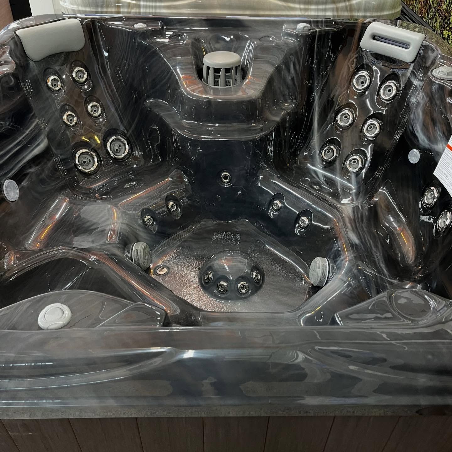 Empty black hot tub with multiple jets and cup holders under clear protective covering