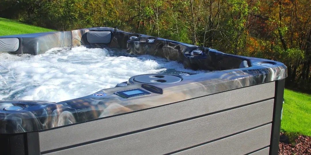 Gray hot tub with bubbling water outdoors beside green grass and trees