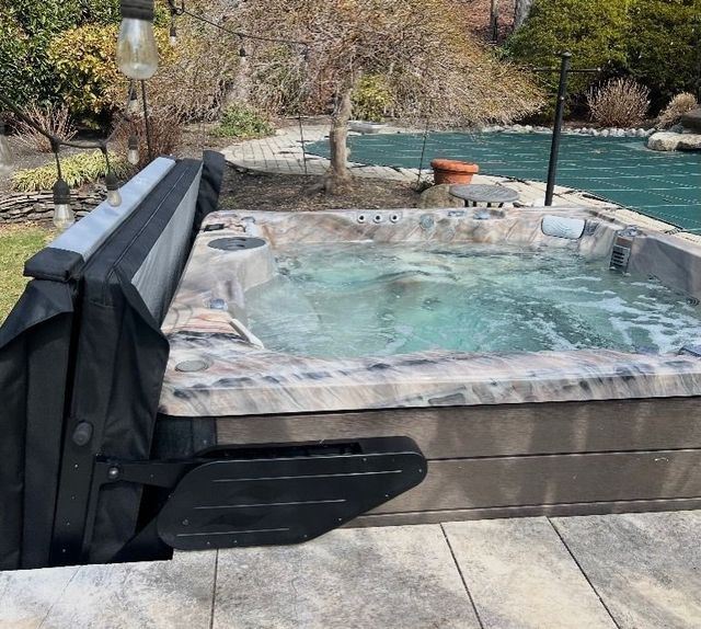 Outdoor hot tub beside a swimming pool with a black cover and snowy mountains in the background