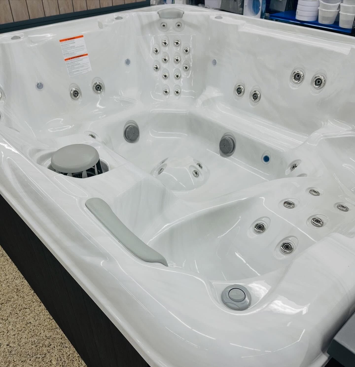 White corner hot tub with multiple jets and gray headrests in a showroom setting