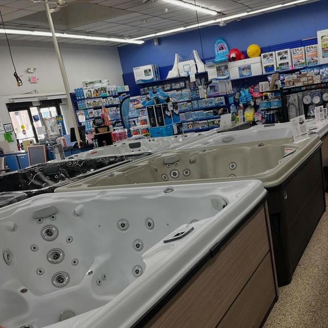 Display of hot tubs in a store showroom with blue walls and pool accessories in the background