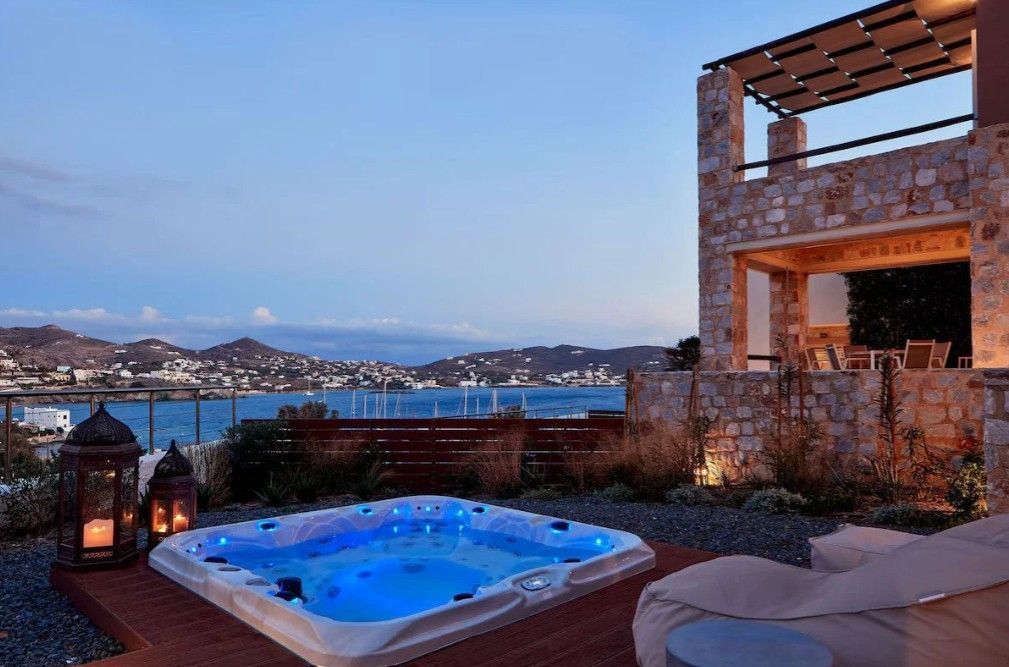 Luxury patio with glowing hot tub, stone terrace, lanterns, and sea-view at dusk