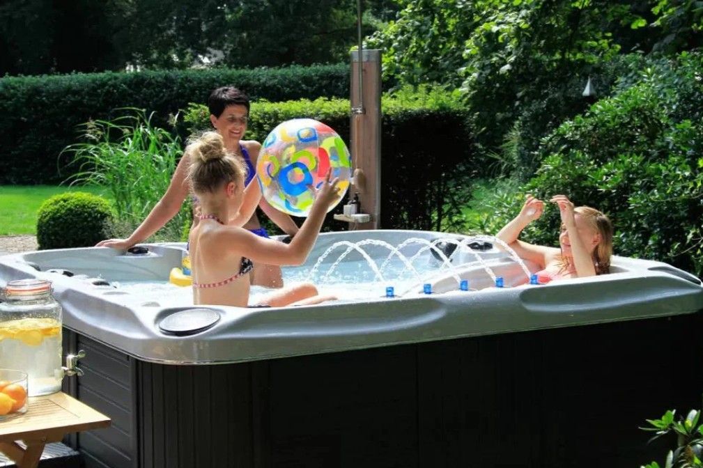 Children playing in a backyard hot tub with a colorful beach ball