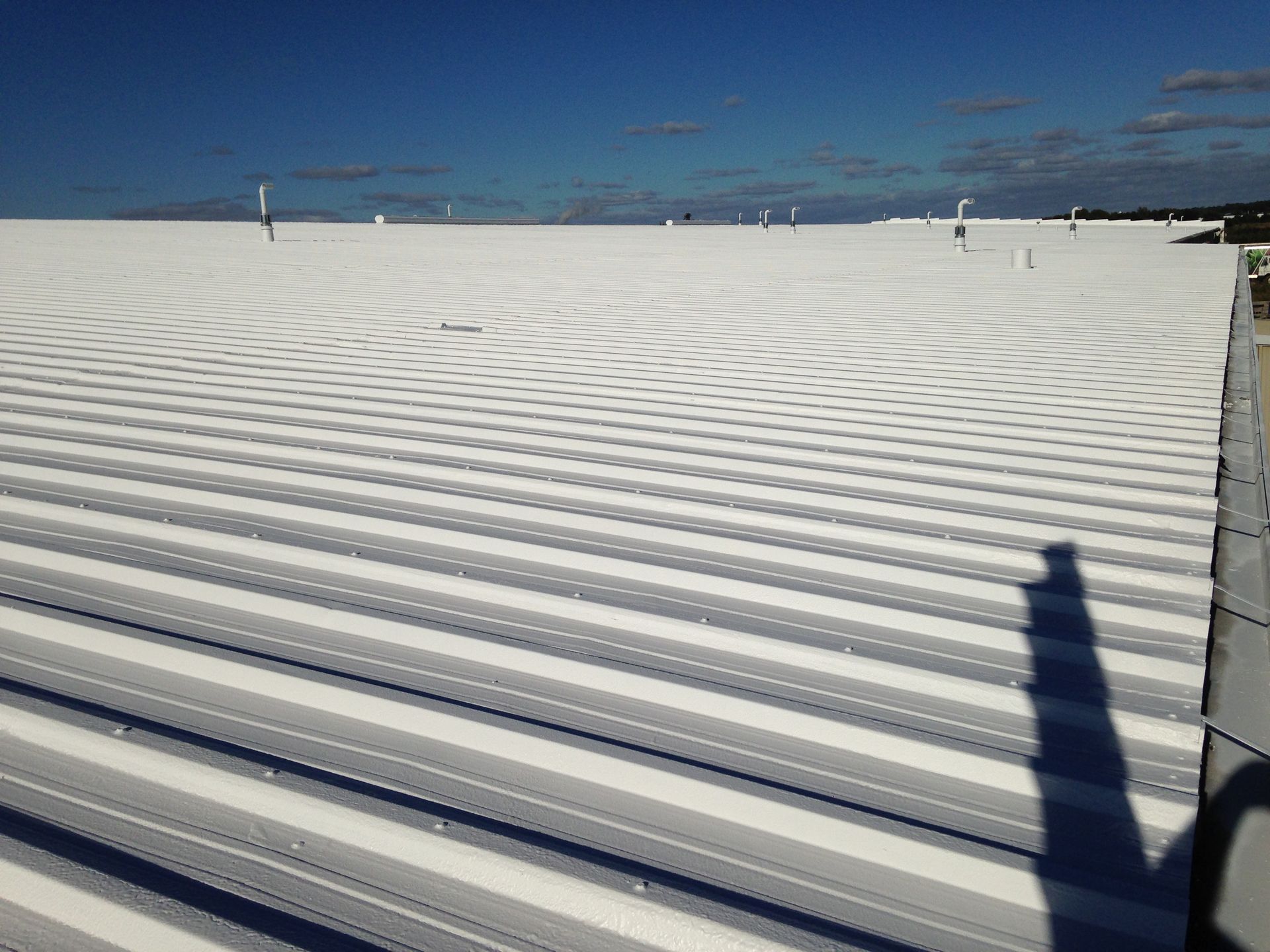 White corrugated metal roof under a clear blue sky. Shadow of the photographer is visible.