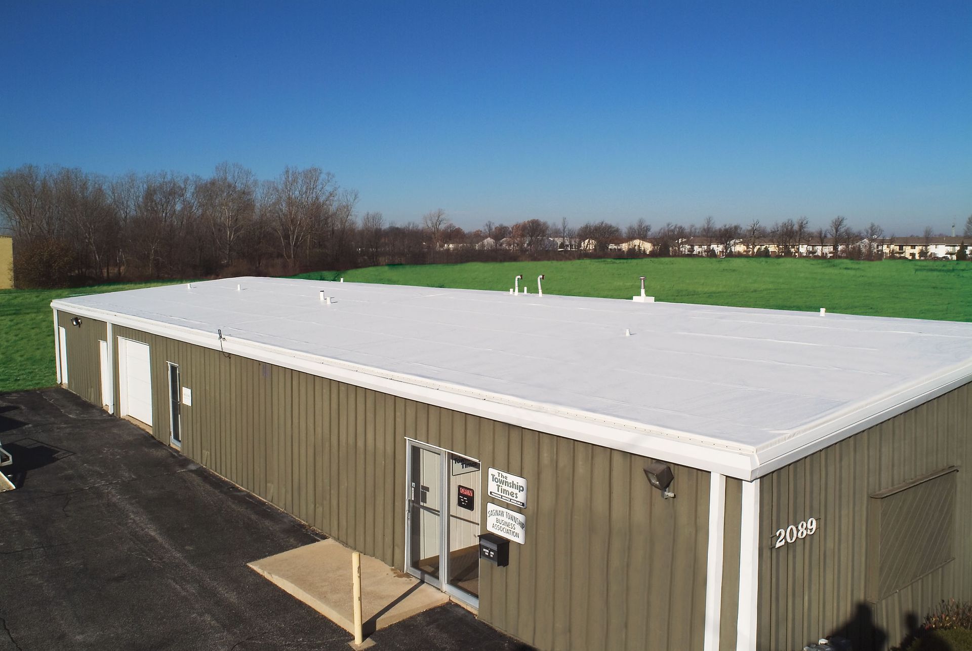 Exterior of a low, industrial building with a white roof. Green grass and blue sky in the background.
