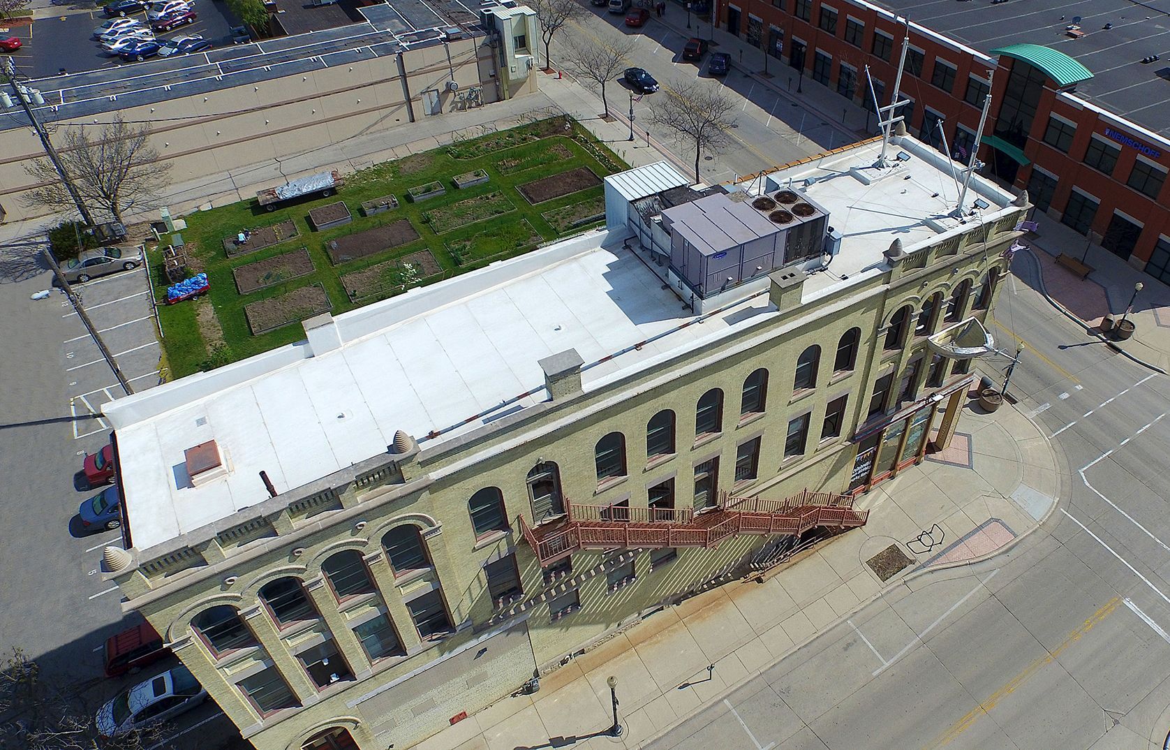 Aerial view of a tan multi-story building with a flat white roof and a small garden.
