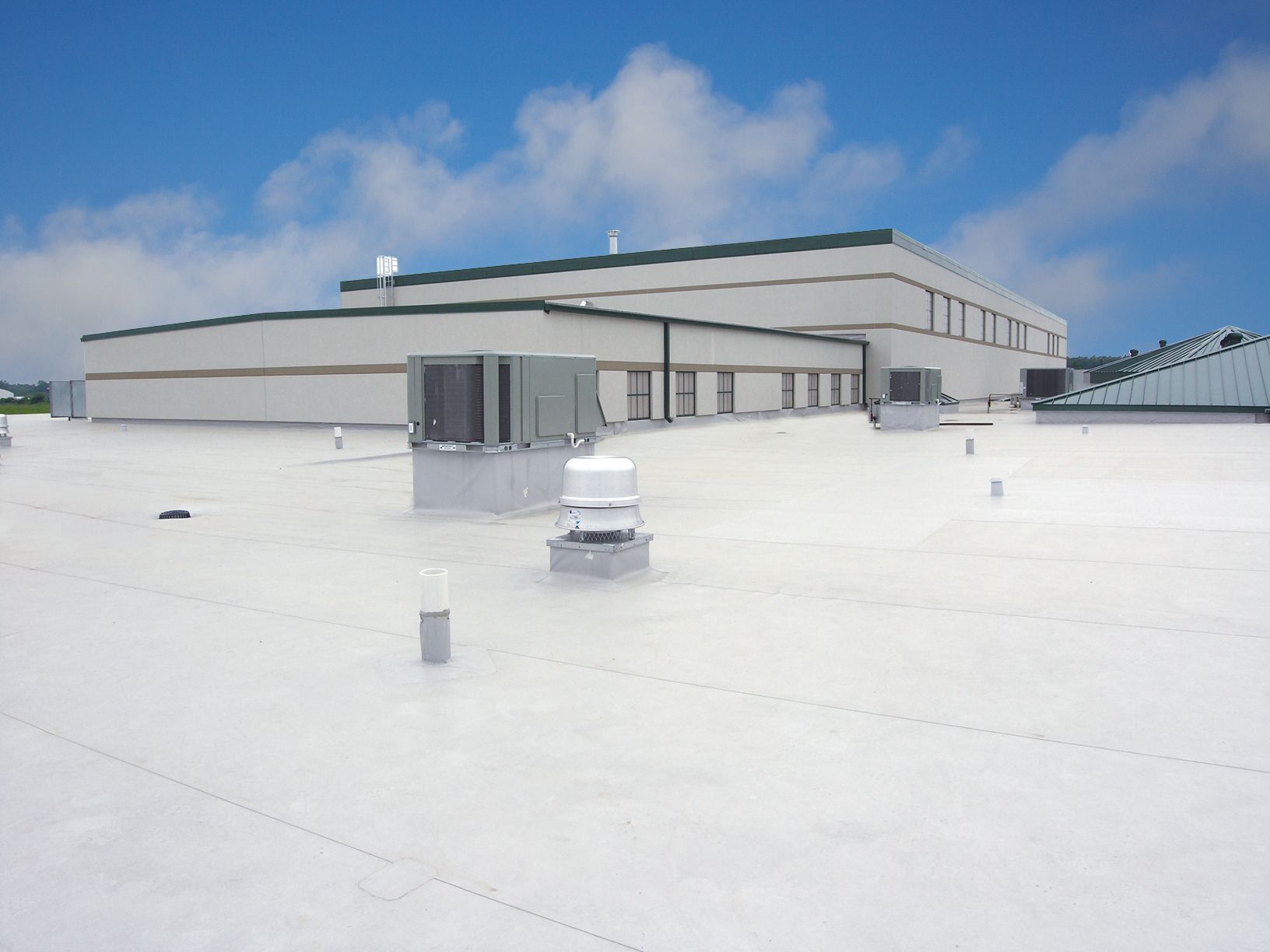 White commercial roof with HVAC units, vents, and a building against a partly cloudy blue sky.