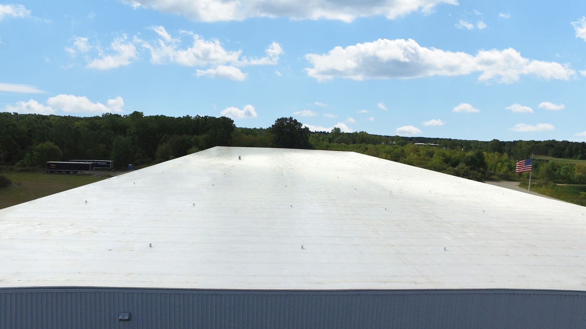 Wide shot of a warehouse roof with a blue sky and scattered clouds.