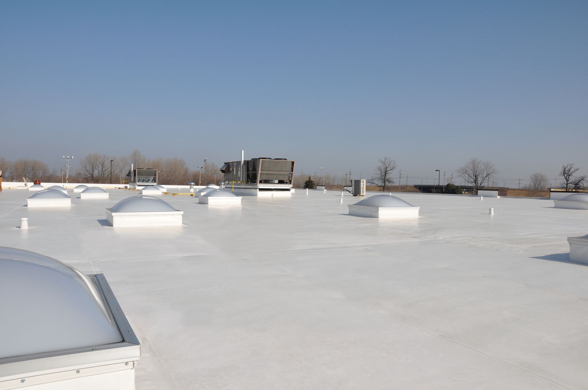 White commercial roof with skylights under a clear, blue sky.