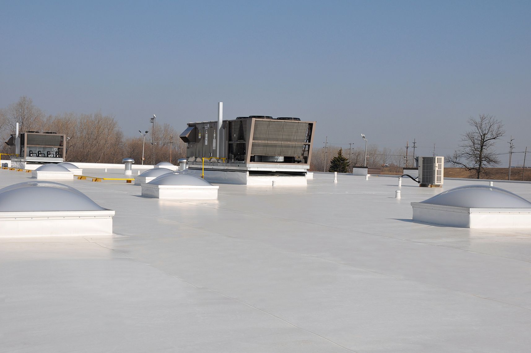 White commercial roof with skylights and HVAC units under a blue sky.
