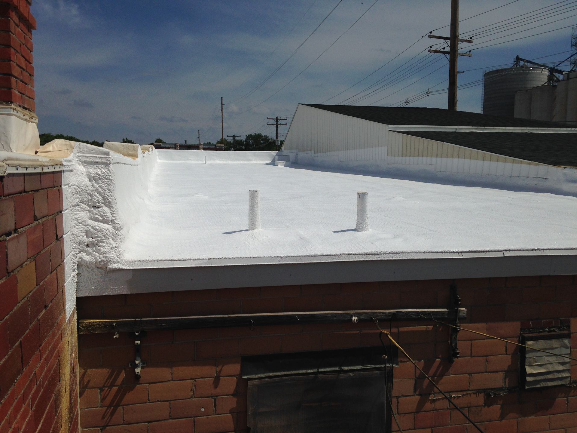 White coated flat roof on a brick building with chimney and blue sky backdrop.
