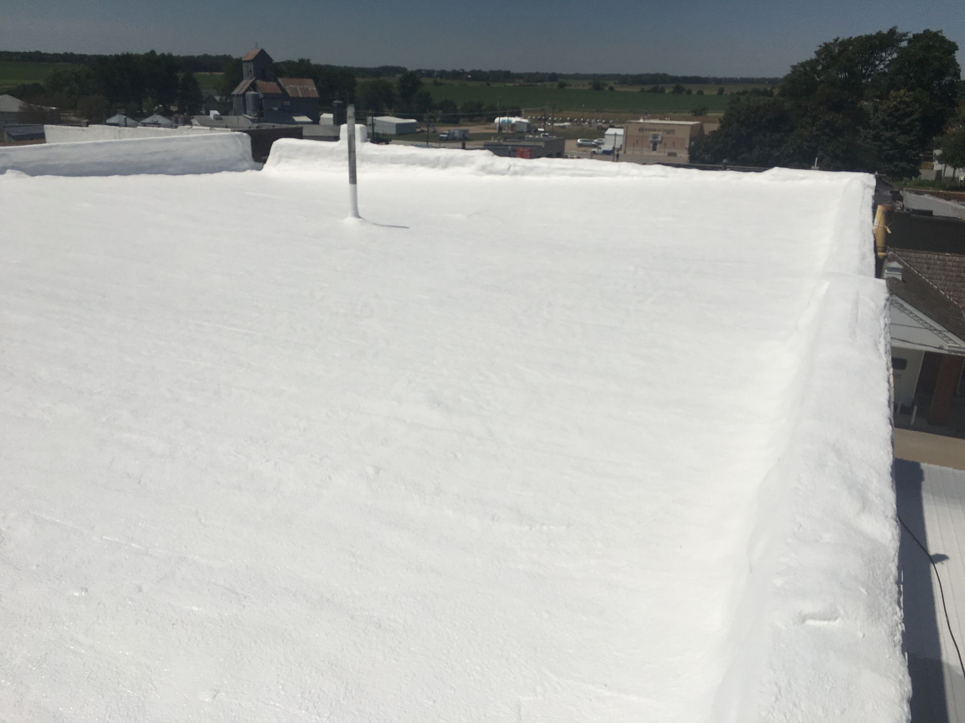 White-coated flat roof; distant buildings and landscape in background, sunny day.