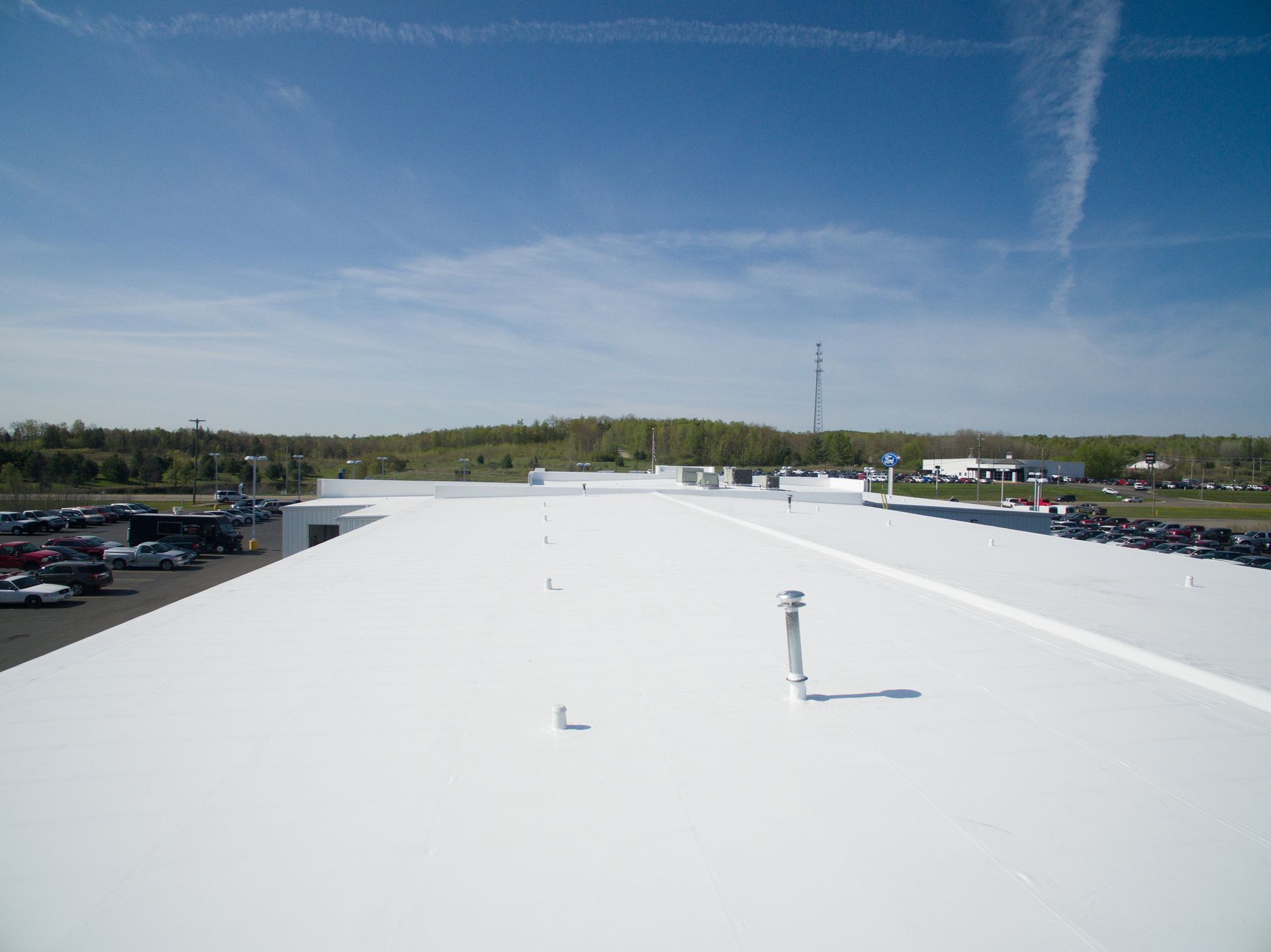 White commercial roof on a sunny day with trees in the background and a few cars parked.