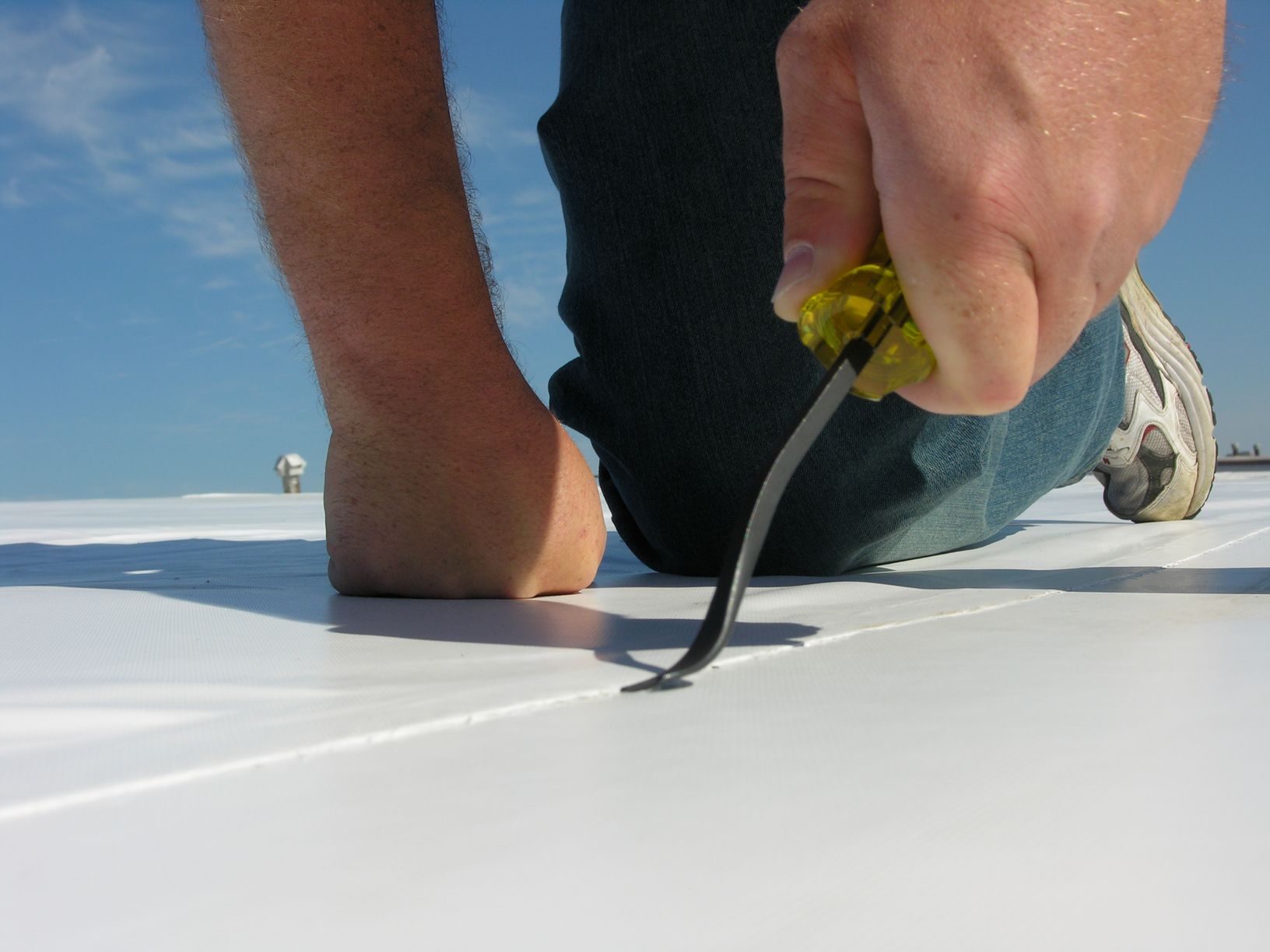 Person kneeling on a white surface using a curved tool to pry something up.