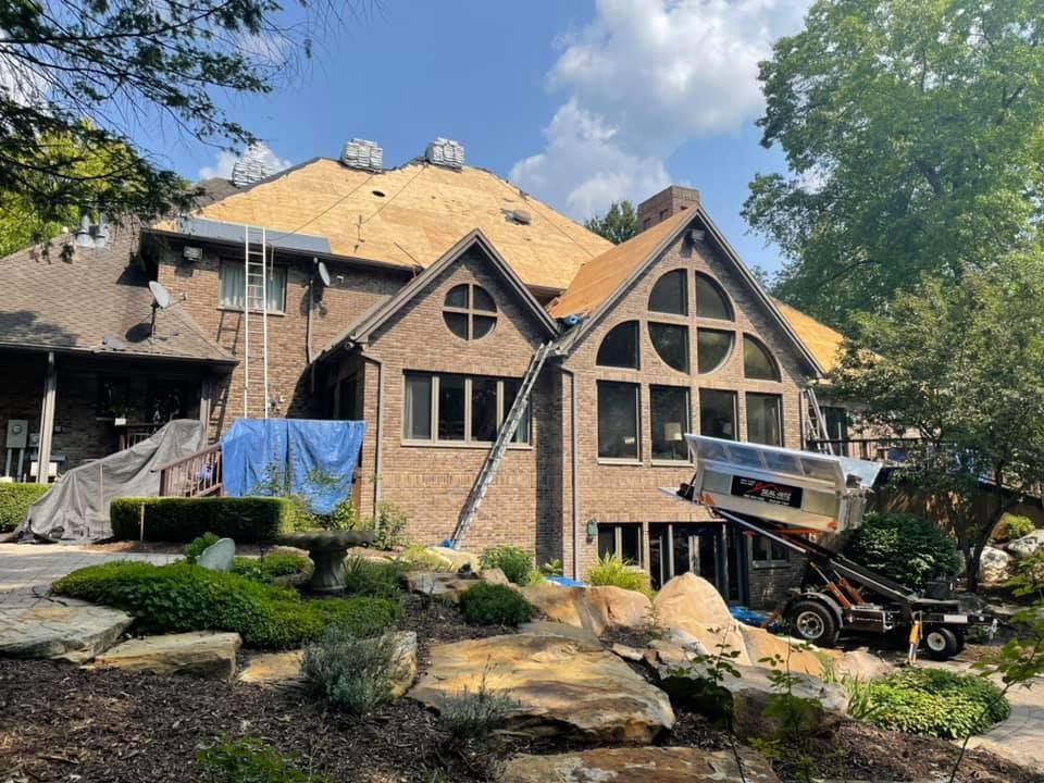 House with exposed roof undergoing repair, surrounded by landscaping and construction equipment.