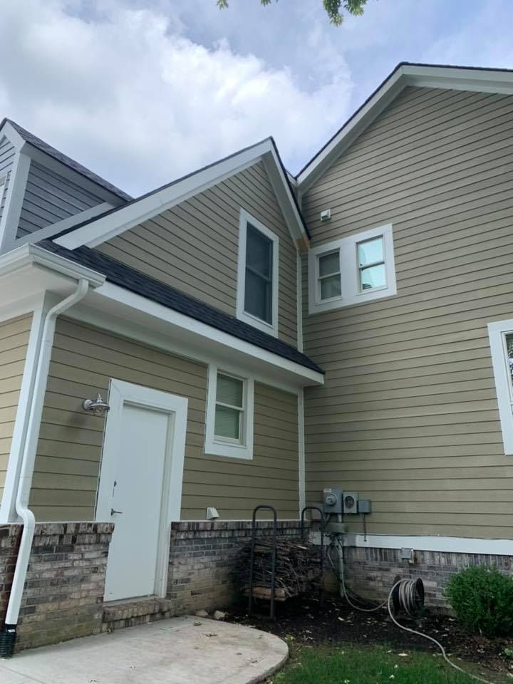 Exterior view of a house with tan siding, white trim, and a black roof.