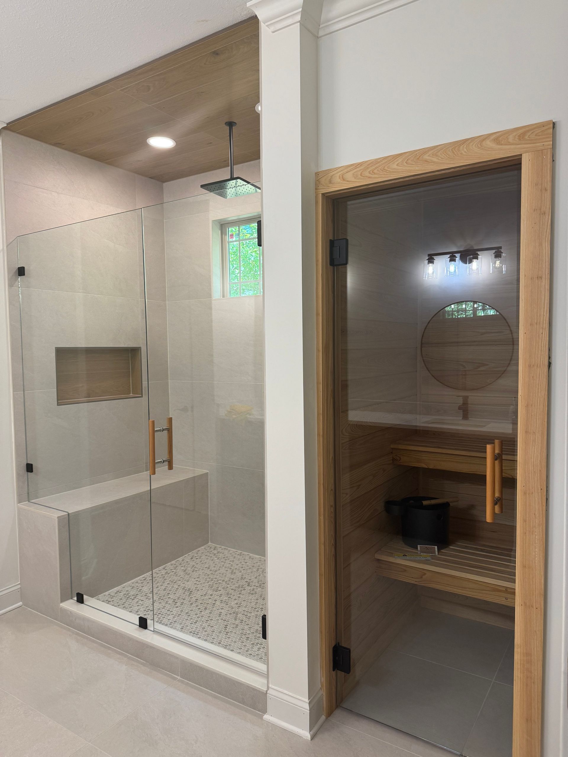 Bathroom with glass shower, white tile walls, and a wooden vanity with round mirror.