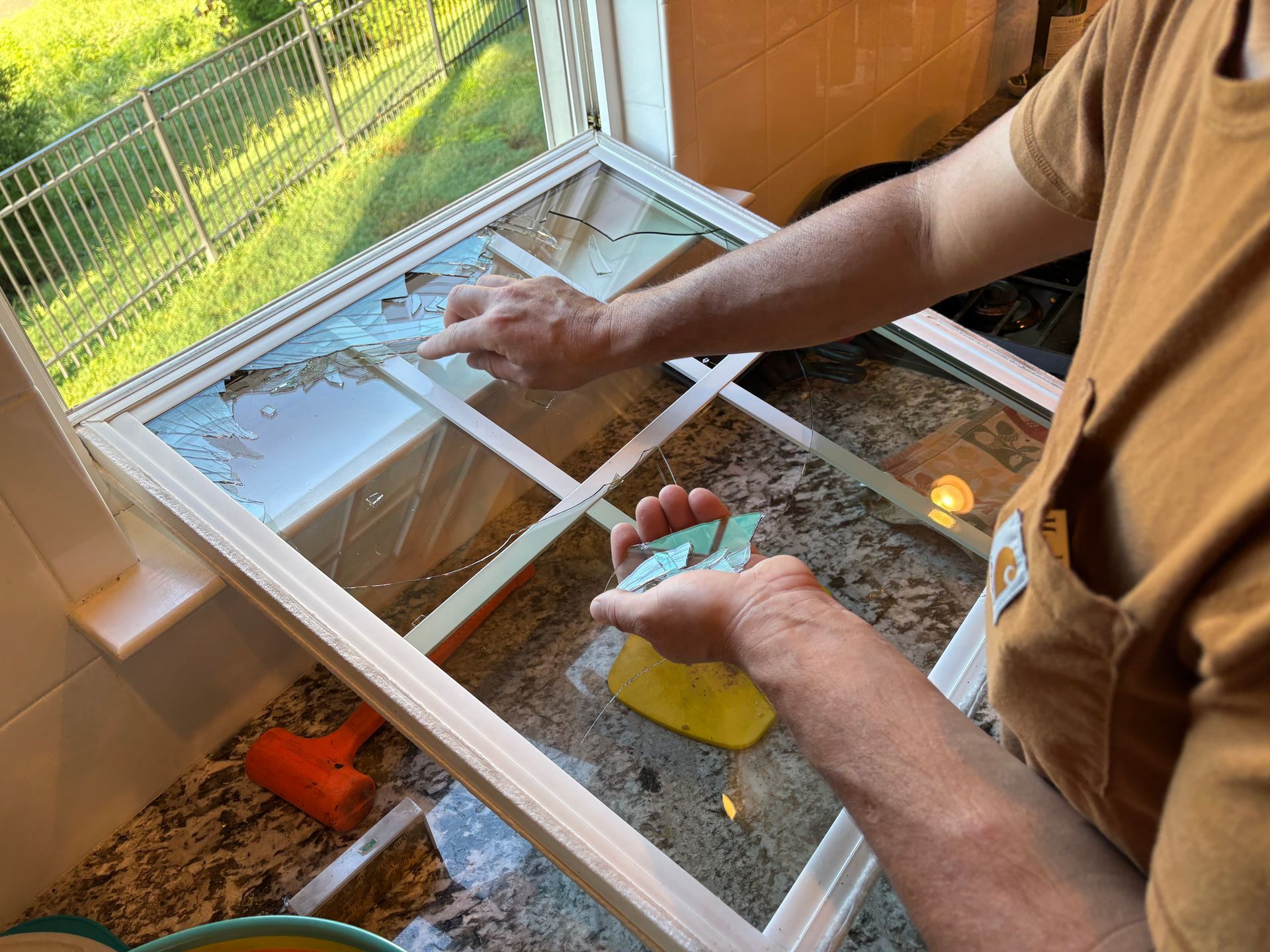 Person cleaning a windowpane with a yellow sponge beside a screened porch door