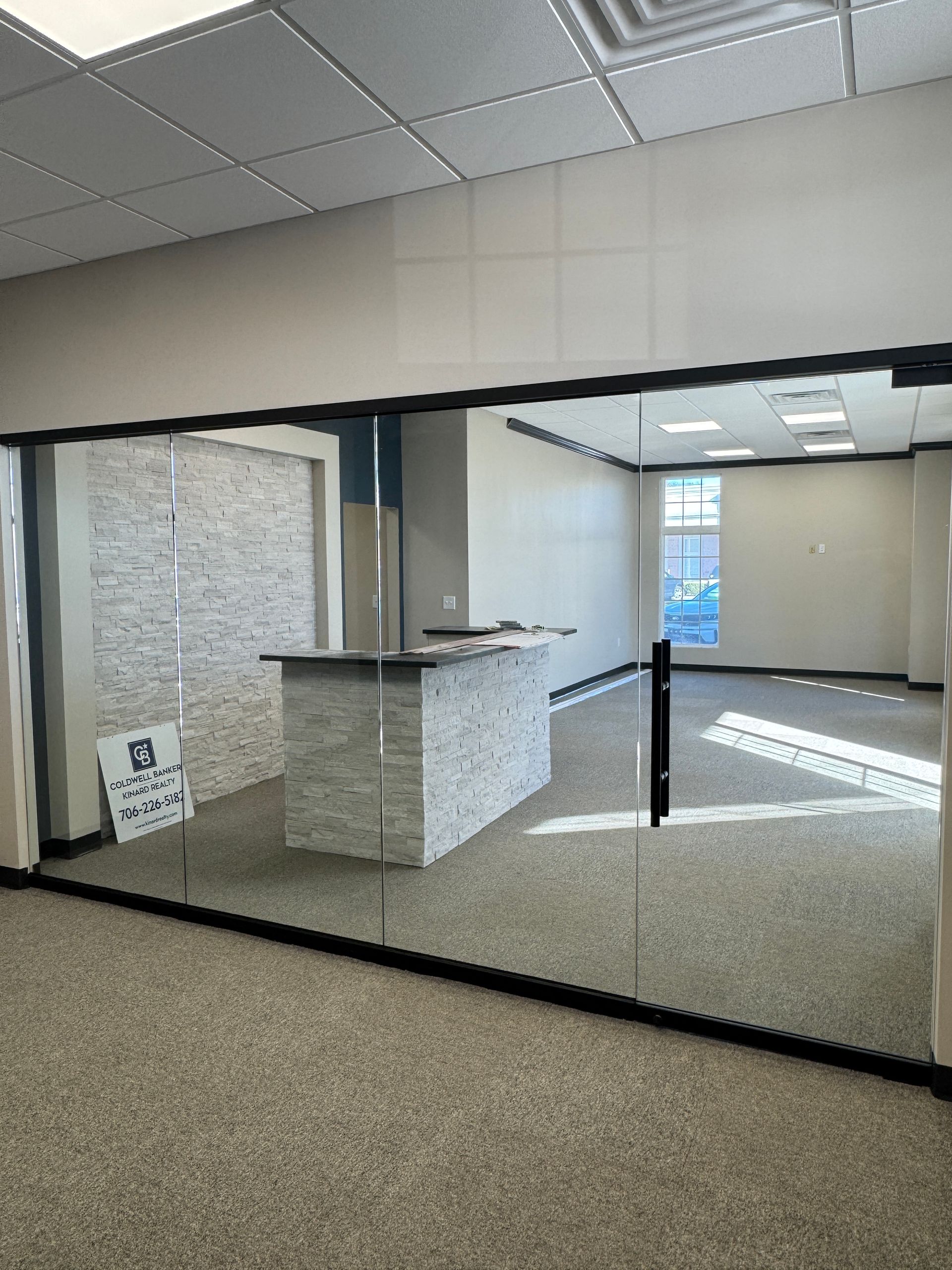 Empty office lobby with glass walls, carpeted floor, and a small reception counter