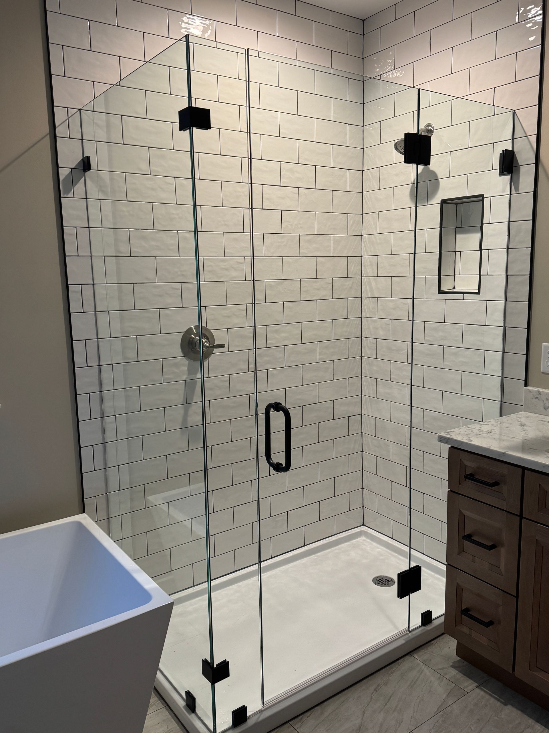 Glass walk-in shower with black hardware, white tile walls, and a built-in shower bench