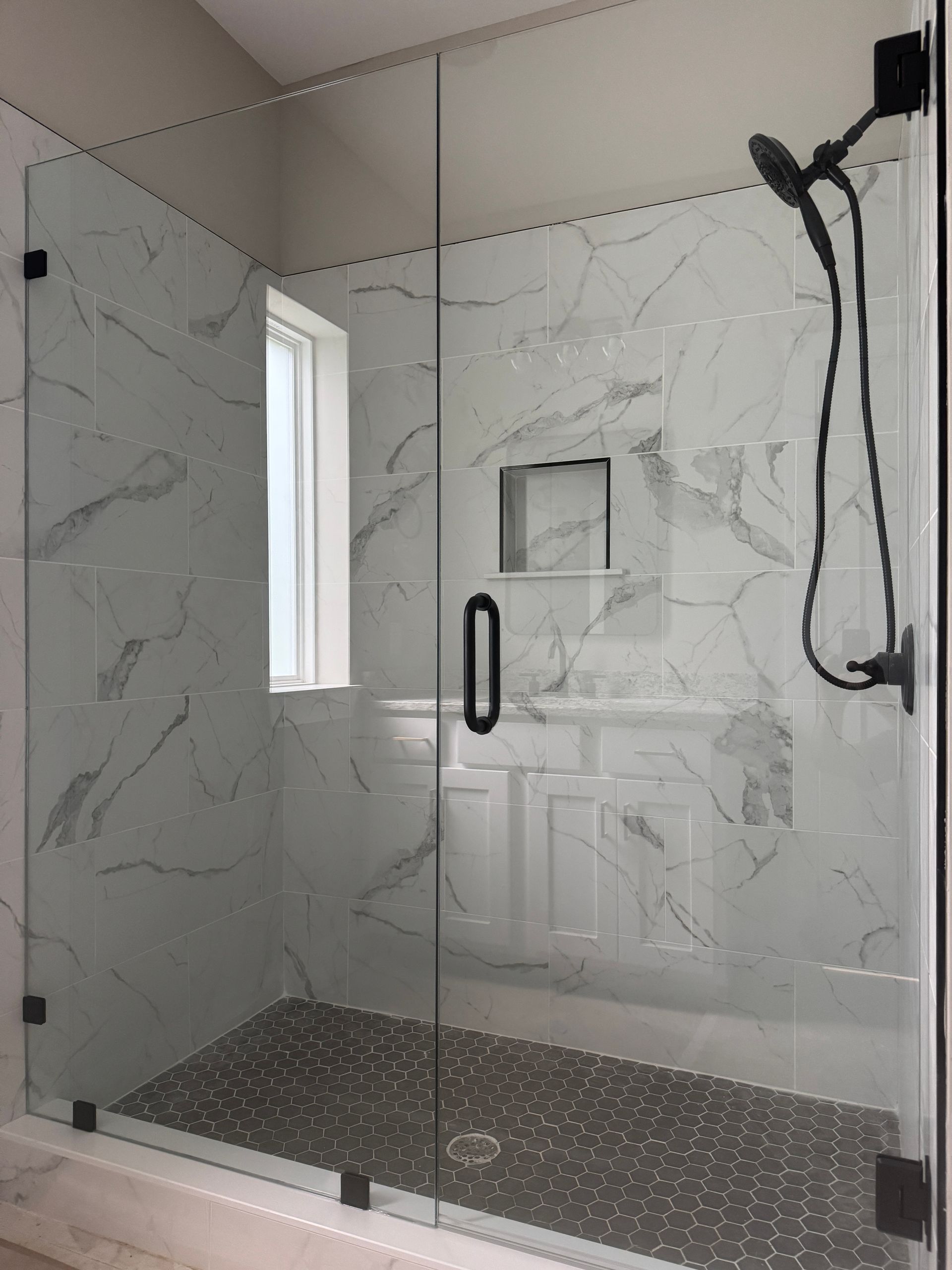 Modern walk-in shower with marble walls, glass enclosure, pebble floor, and black fixtures