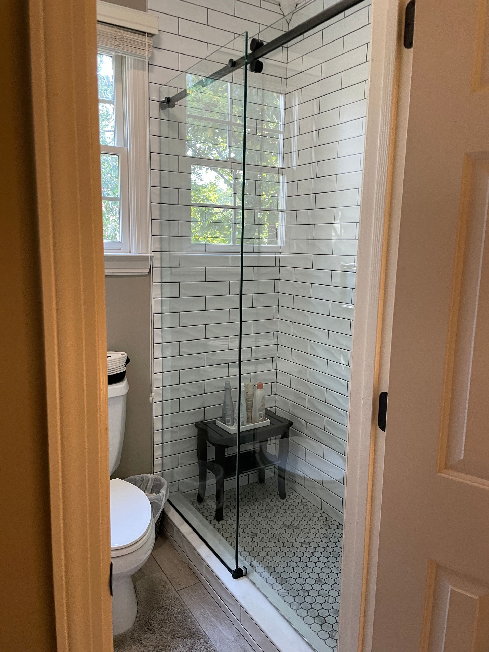 Small bathroom with a glass shower enclosure, tiled walls, toilet, and window with daylight.