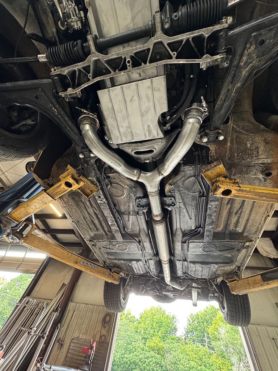 Undercarriage of a car on a lift, showing exhaust and drivetrain components in a repair shop.