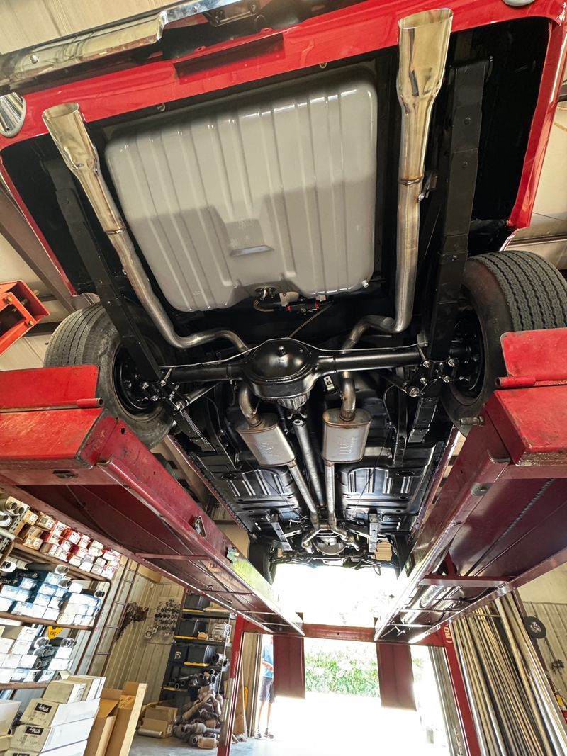 Undercarriage of a red car on a lift in an auto shop, showing exhaust and suspension components