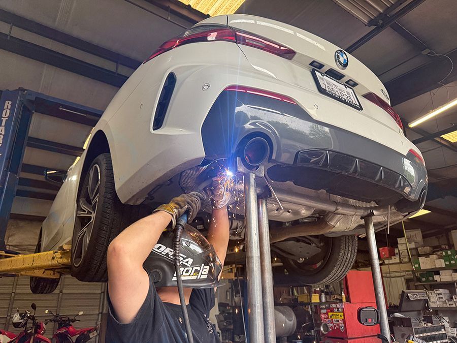 Mechanic welding under a white car on a lift in an auto repair shop, sparks flying.