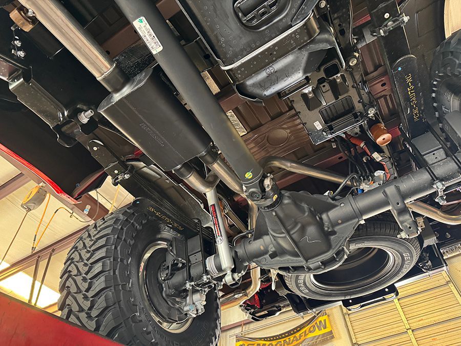 Undercarriage of a vehicle on a lift, showing tires, suspension, and exhaust components.