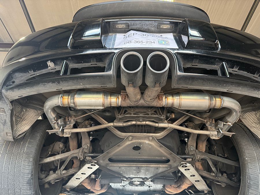 Rear underside of a black sports car, showing dual exhaust, suspension, and chassis details