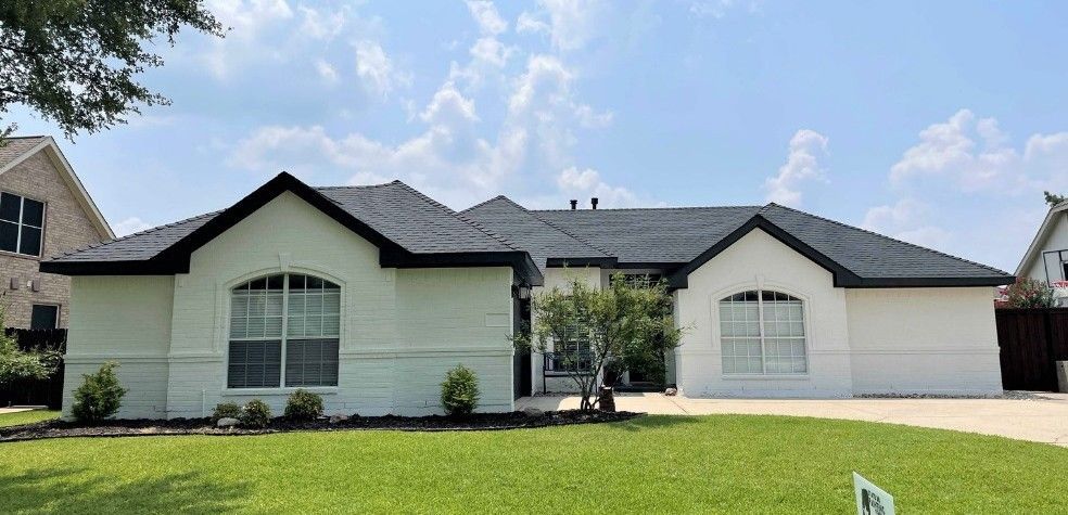 A white house with a black roof is sitting on top of a lush green lawn.