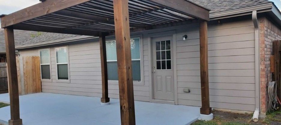 A small house with a wooden pergola in front of it.