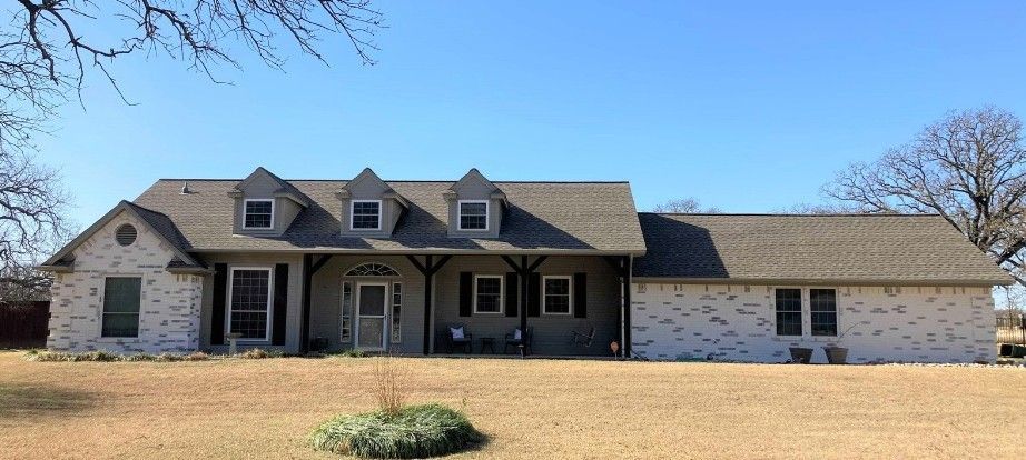 A large white brick house with a gray roof is sitting in the middle of a grassy field.