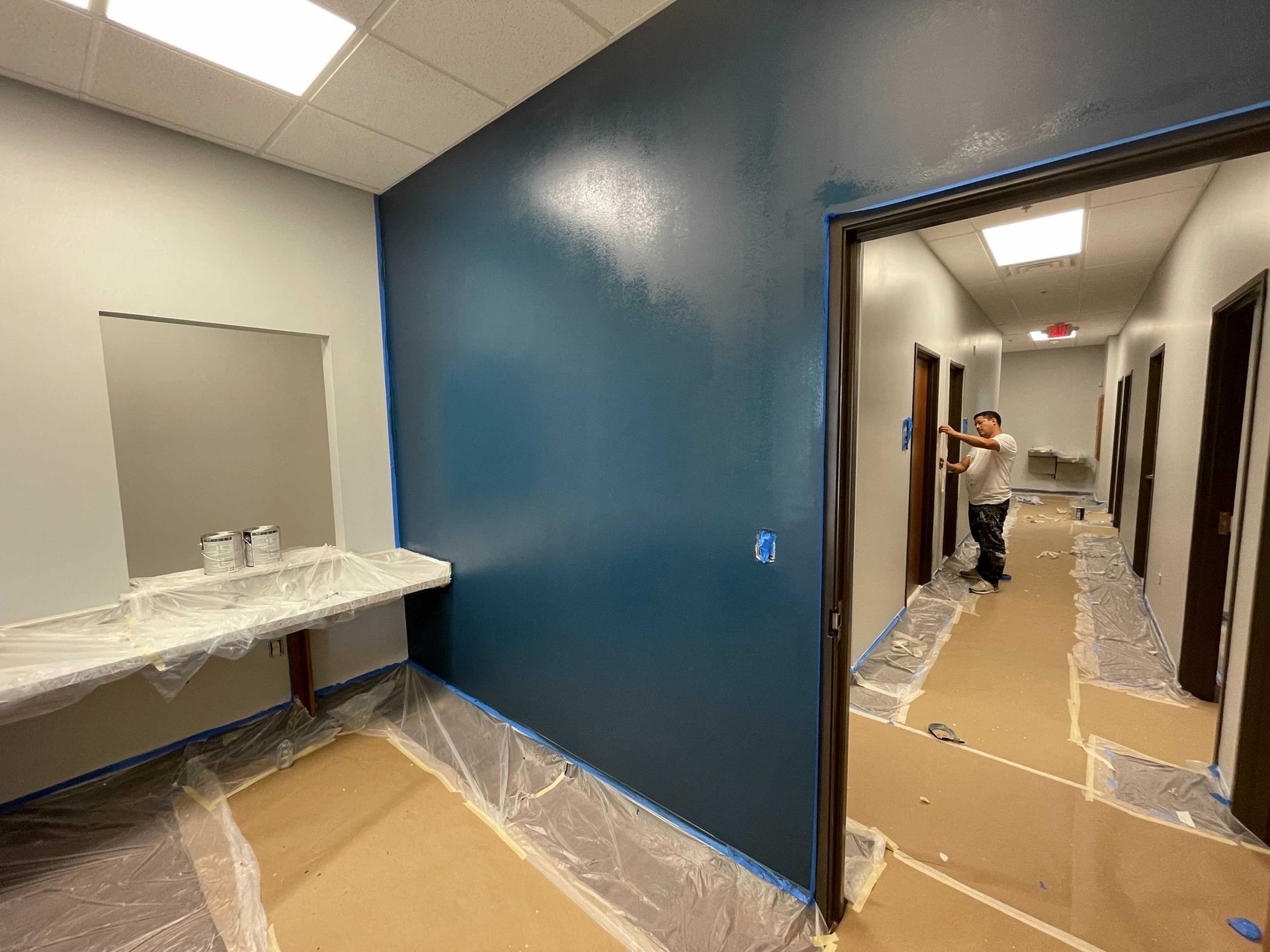 A man is painting a blue wall in a hallway.