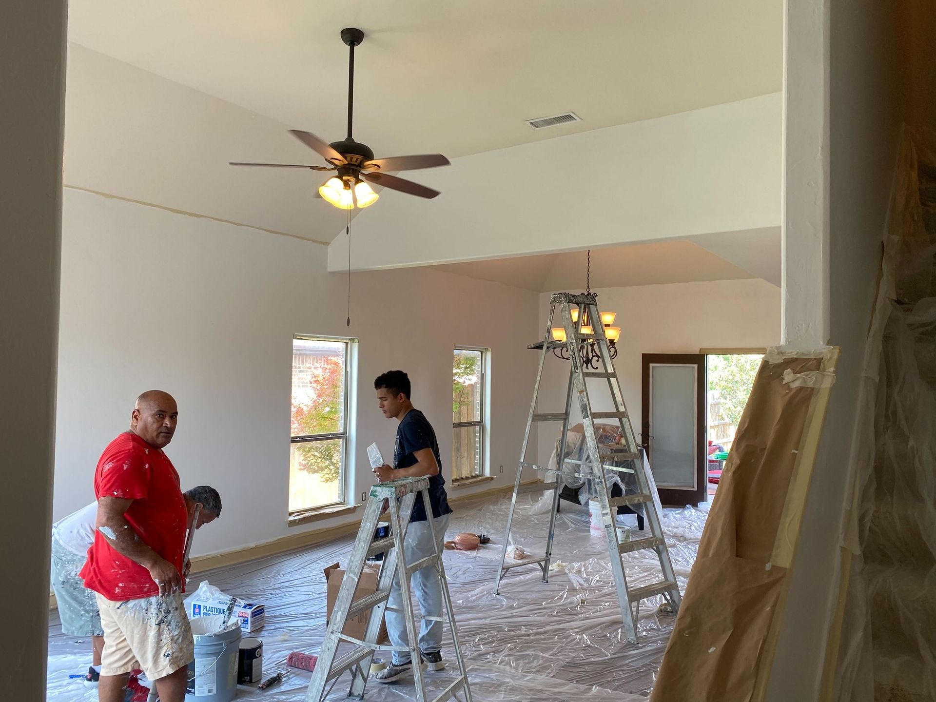 Two men are painting a room with a ceiling fan.