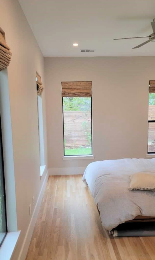 A bedroom with a bed , ceiling fan , and two windows.